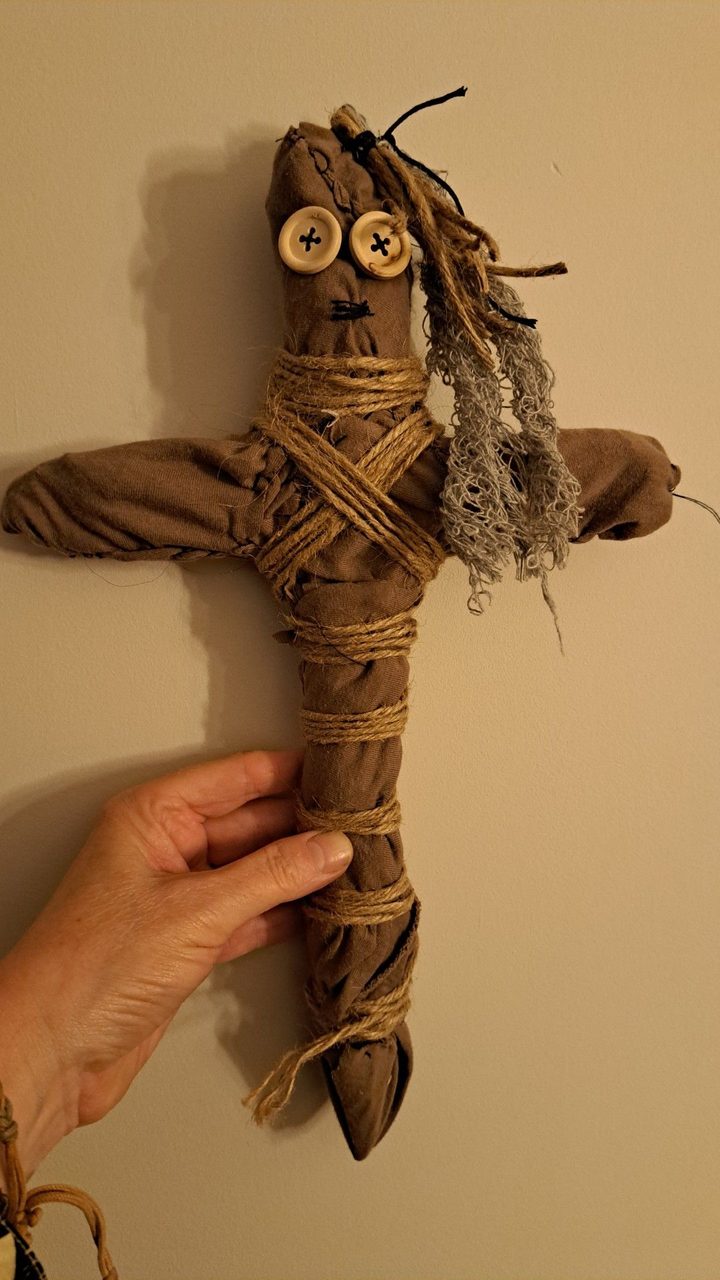A hand holding a cloth doll bound with twine, with button eyes and hair made of plant fibre