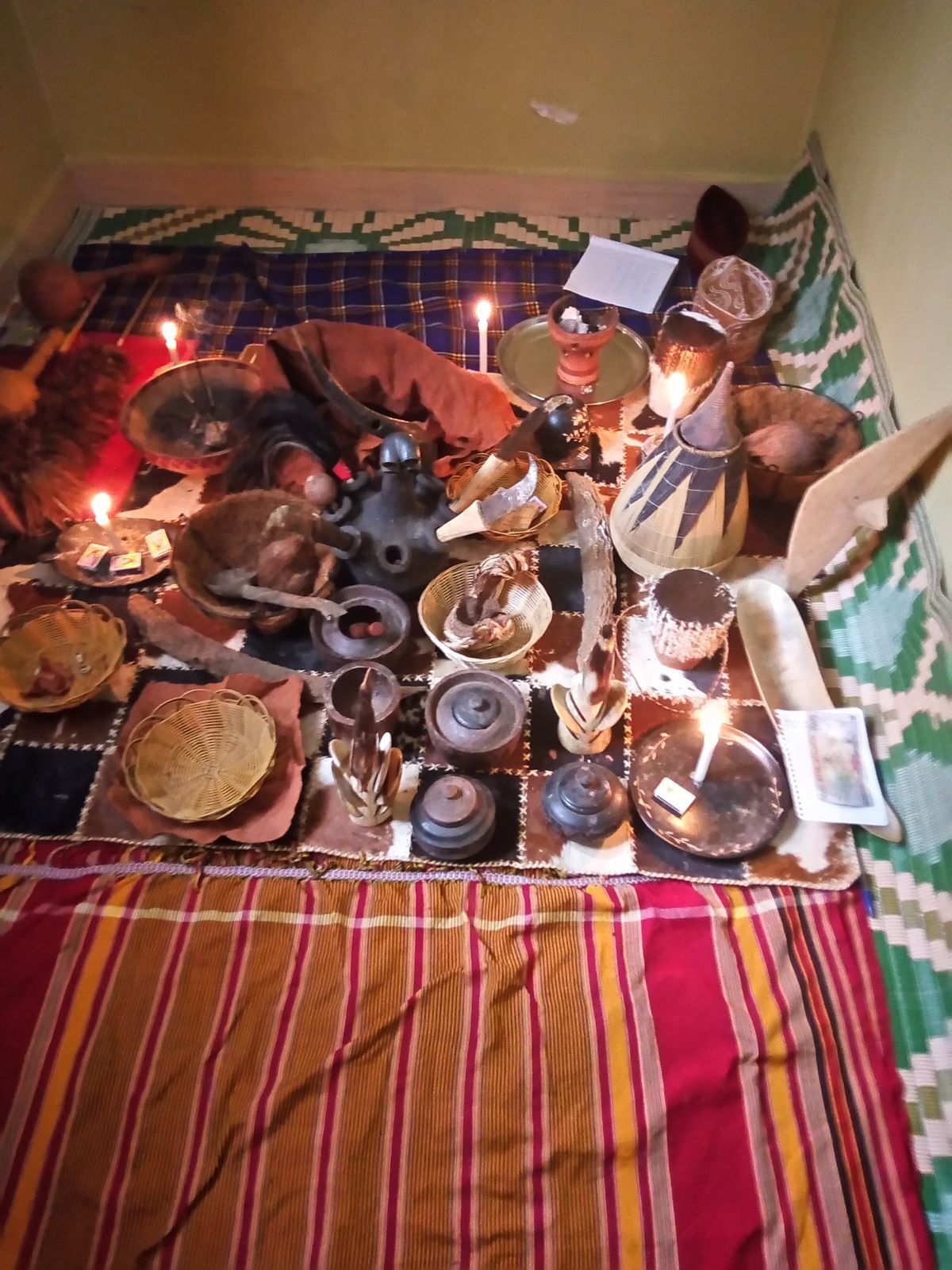 Ritual bowls, objects and lit candles laid out on patterned cloth