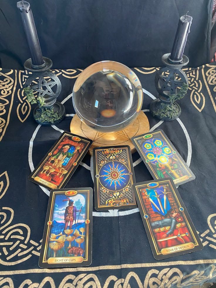 Tarot cards laid out around a crystal ball, between two black candles on a black and gold cloth
